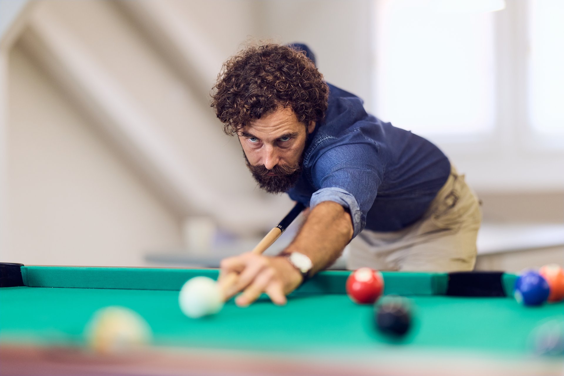 Man playing billiards with focus, aiming carefully on a well-lit indoor pool table