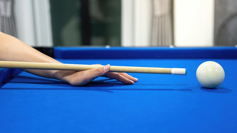Close-up of hand aiming cue stick at white cue ball on blue billiard table, focused shot