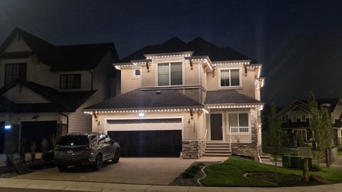 Two-story residential home with exterior lighting at night, featuring a dark garage door and landscaped front yard