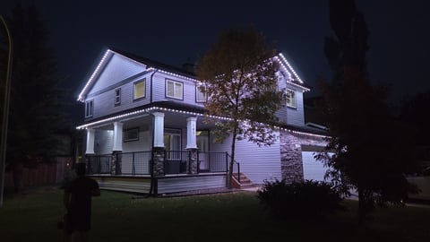 Two-story white house illuminated at night with front porch, surrounded by dark trees and lawn