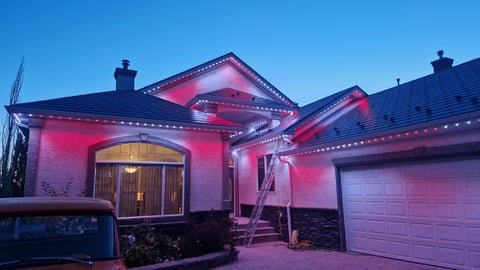 Modern single-story house illuminated with pink and red LED lights at dusk, featuring arched entrance and garage door