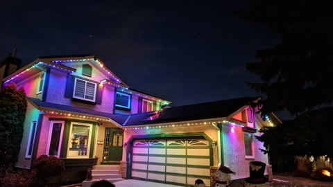 House illuminated at night with colorful neon pink, purple, blue, and yellow lights projecting onto the exterior walls and garage door